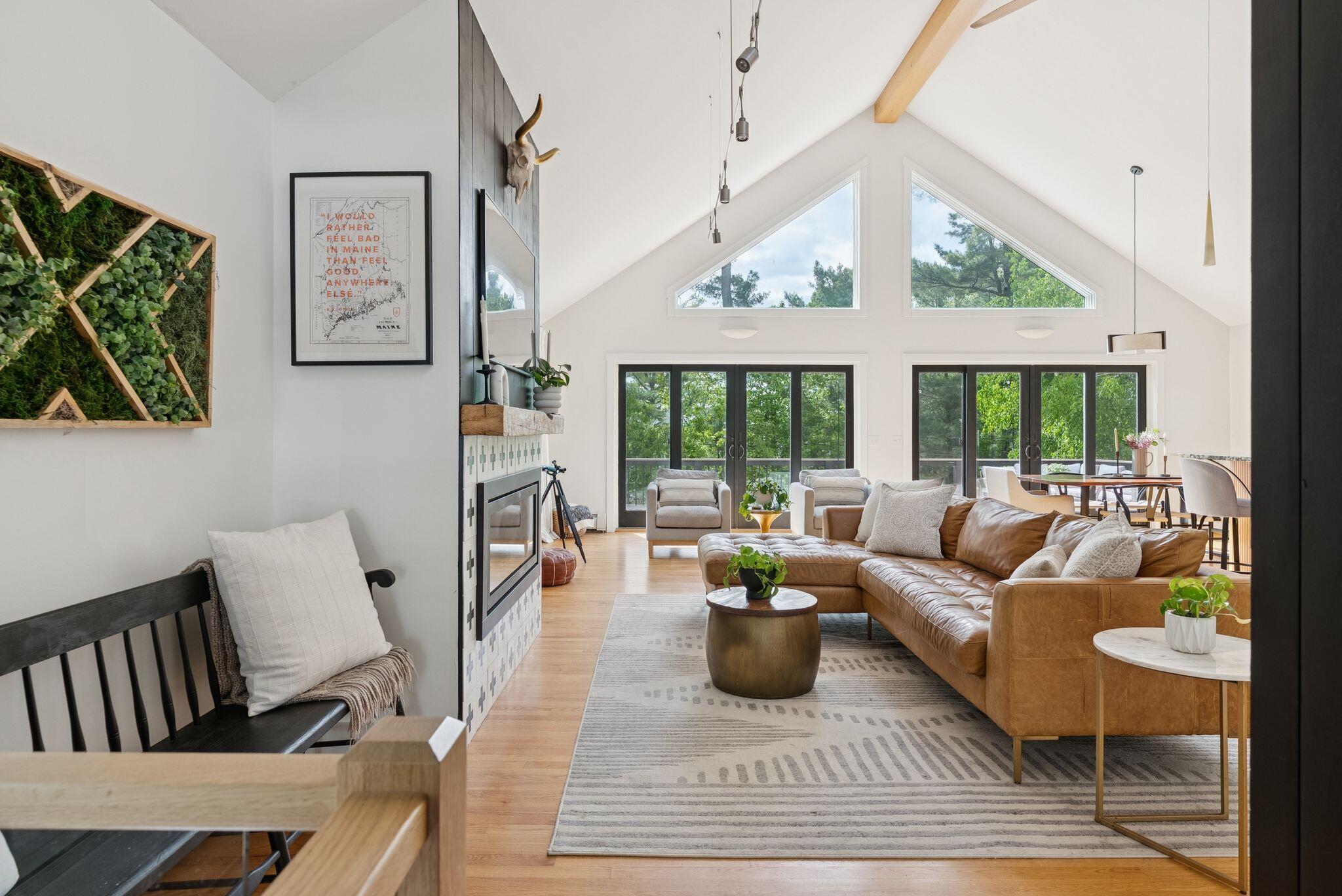 Staged living room with cathedral ceiling, floor-to-ceiling windows, and warm natural light